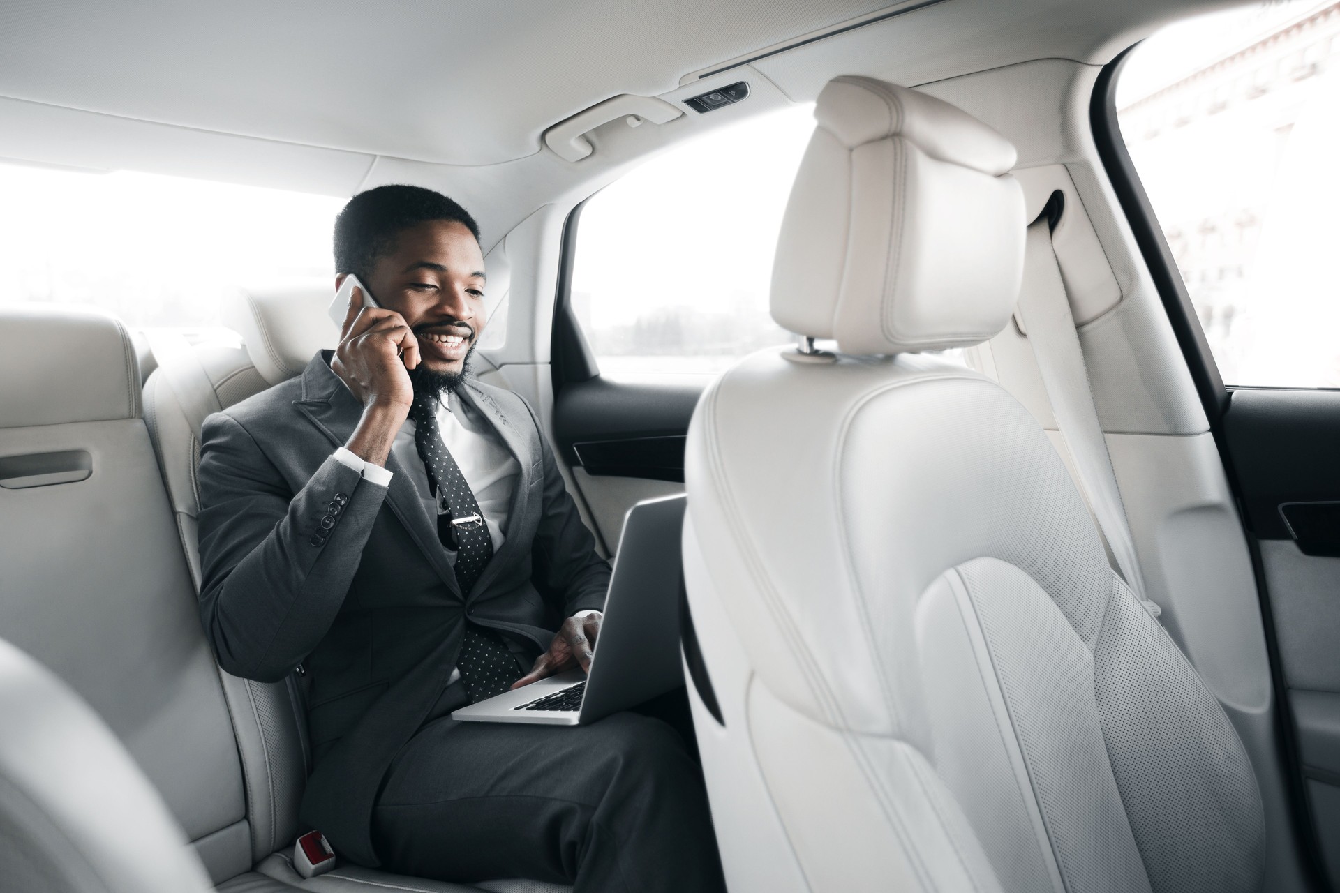 Professional Man Working on Laptop While Making a Phone Call in a Luxury Car
